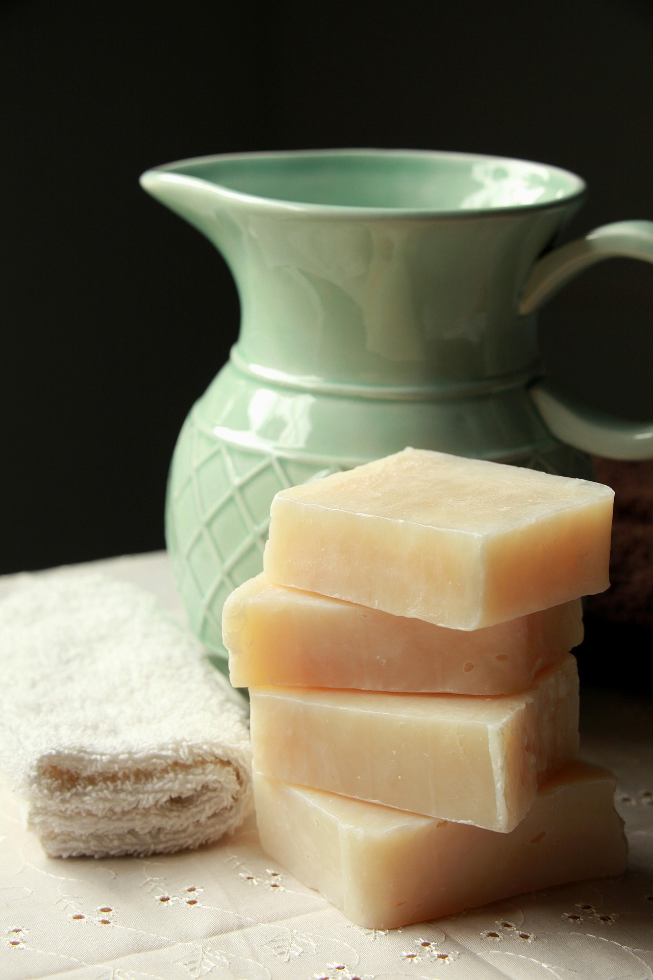 Stack of handmade soap bars beside a ceramic pitcher and towel